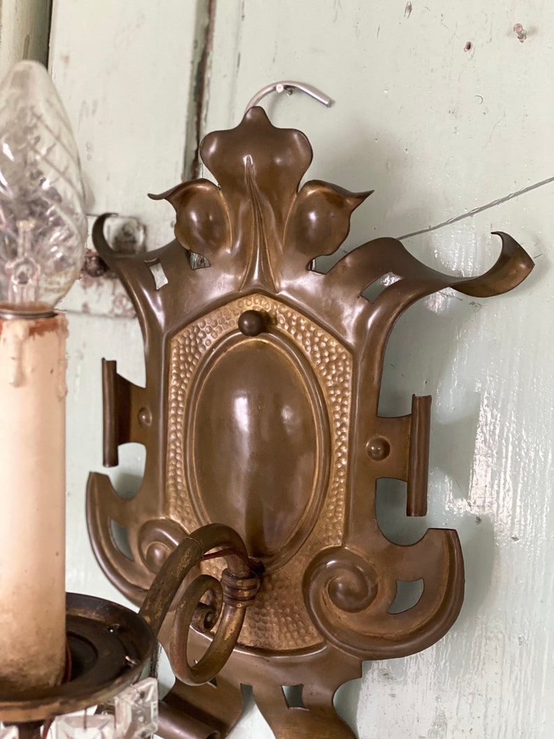 May include: A vintage brass wall sconce with an ornate design. The sconce features a single candle holder and a decorative backplate with a floral motif.