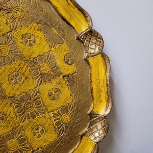Op de afbeelding: Een decoratief dienblad in geel en goud met een bloemenmotief. Het dienblad heeft een gegolfde rand en een verhoogde rand.