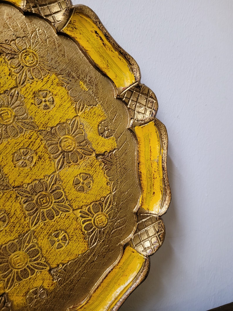 Op de afbeelding: Een decoratief dienblad in geel en goud met een bloemenmotief. Het dienblad heeft een gegolfde rand en een verhoogde rand.