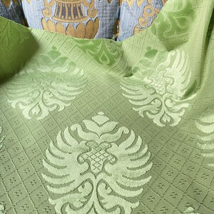May include: Green fabric with a repeating pattern of stylized floral and bird motifs. The fabric has a textured, raised surface.
