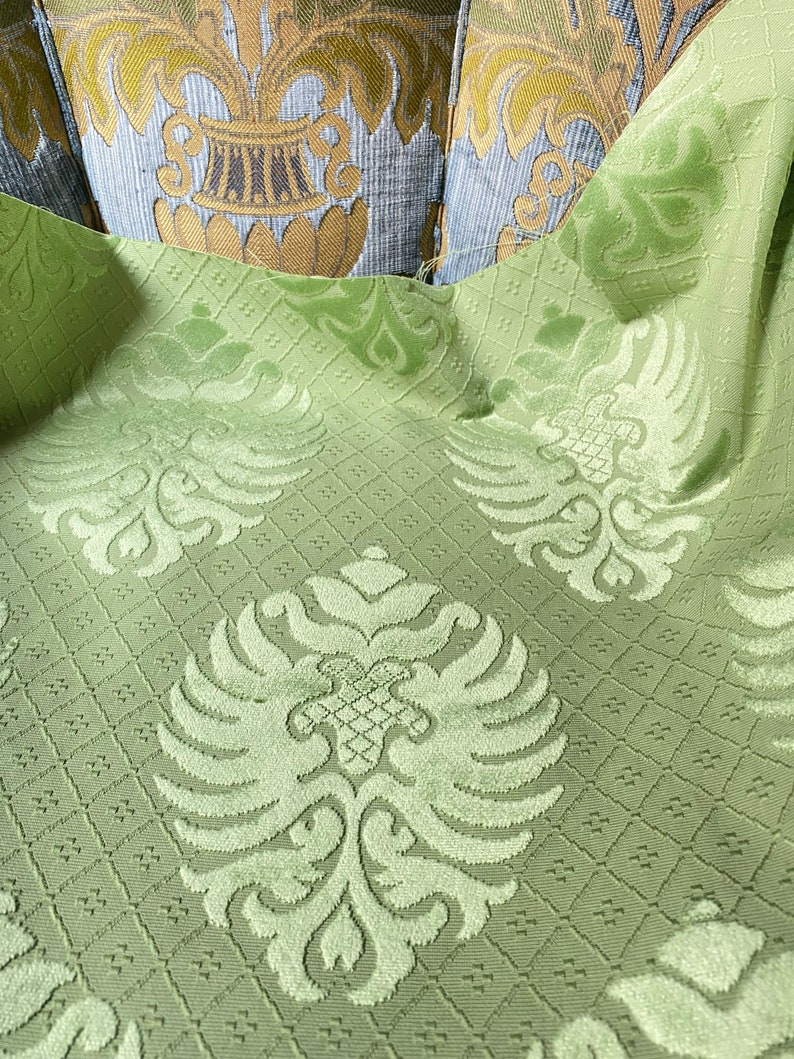 May include: Green fabric with a repeating pattern of stylized floral and bird motifs. The fabric has a textured, raised surface.