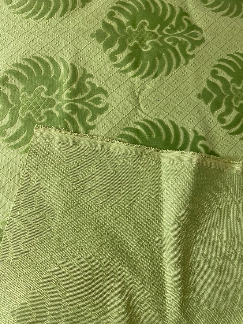 May include: Green fabric with a damask pattern. The fabric has a subtle sheen and a textured surface.