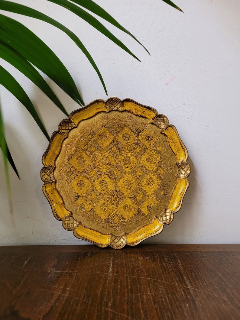 Op de afbeelding: Een ronde, gele, houten dienblad met een decoratief, gesneden ontwerp. Het dienblad heeft een gegolfde rand en een verhoogd midden.