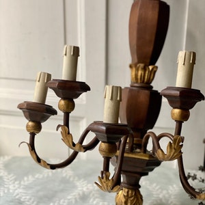 May include: A wooden wall sconce chandelier with five candle-style light bulbs. The chandelier is painted brown with gold accents and has a scrolled metal frame.
