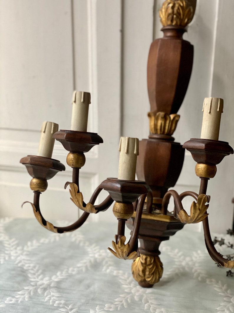 May include: A wooden wall sconce chandelier with five candle-style light bulbs. The chandelier is painted brown with gold accents and has a scrolled metal frame.