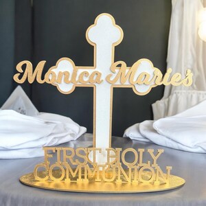 May include: Gold glitter cross with the name "Monica Marie's" on it. The cross is on a gold glitter base with the words "First Holy Communion" on it.