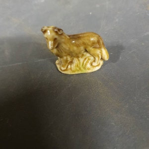 Puede incluir: Una figurita de cerámica marrón de un perro sentado sobre una base verde.