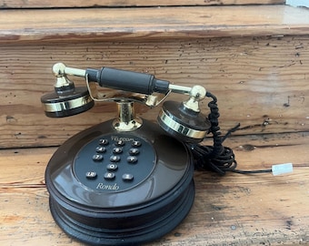 May include: A vintage brown and gold telephone with a rotary dial and a handset. The phone has a round base and a black cord. The word "Telecom" is above the buttons and "Rondo" is printed on the dial.