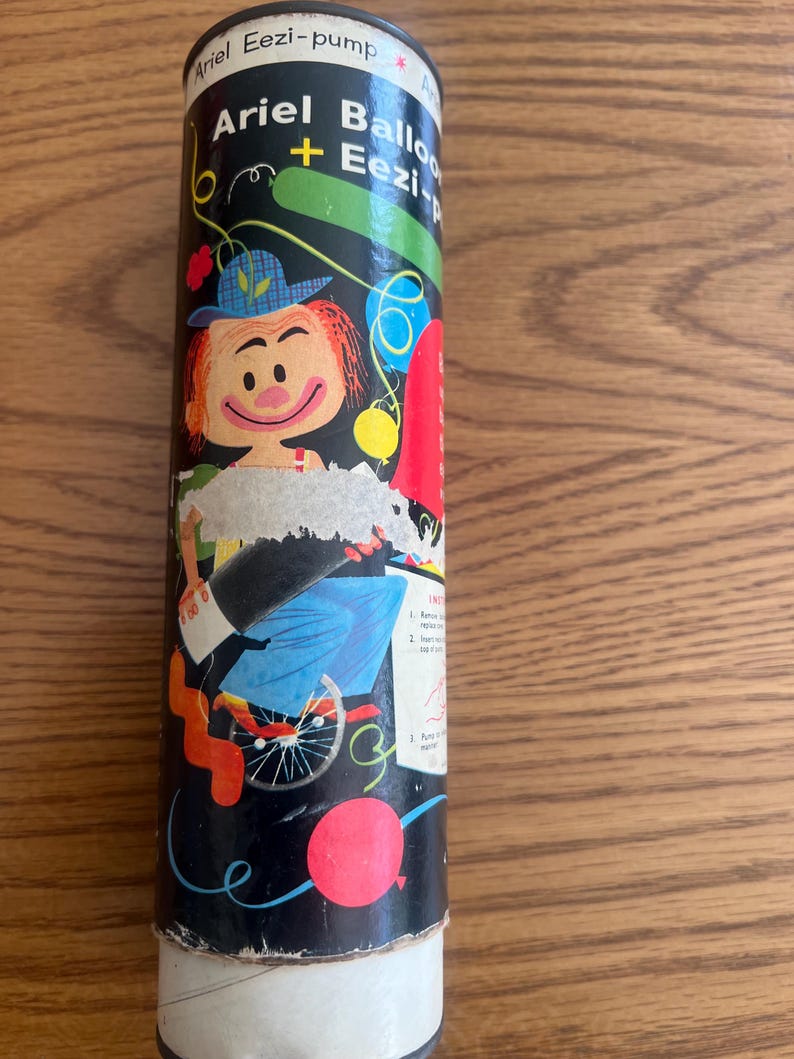 Puede incluir: Un recipiente cil&iacute;ndrico para un inflador de globos Ariel Eezi-pump. El recipiente es negro con una ilustraci&oacute;n de dibujos animados de un payaso y globos. El texto "Ariel Balloon + Eezi-pump" est&aacute; impreso en el recipiente.