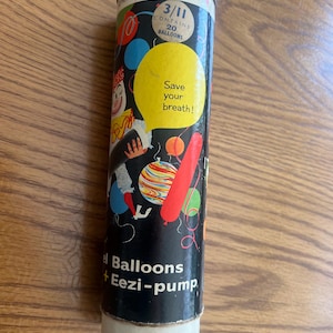 Puede incluir: Un recipiente cil&iacute;ndrico vintage para globos "Eezi-pump". El contenedor negro presenta ilustraciones de globos coloridos, un payaso y el texto "Save your breath!". Una etiqueta indica que contiene 20 globos.