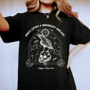 May include: Black t-shirt with a white graphic design featuring a raven perched on a skull with a crescent moon and stars. The text reads "Once upon a midnight dreary" and "Edgar Allan Poe".
