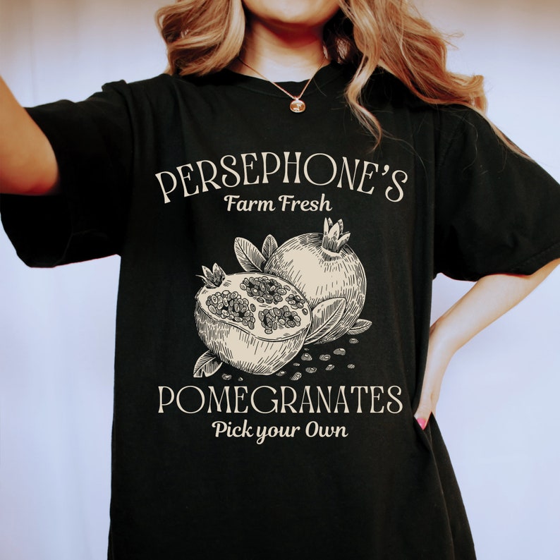 May include: Black t-shirt with a white graphic design that says "Persephone's Farm Fresh Pomegranates Pick your Own". The graphic also features a drawing of two pomegranates.
