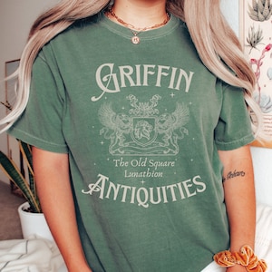 May include: A green t-shirt with a vintage-style graphic of a griffin, a crest, and the text "Griffin The Old Square Lunathion Antiques".