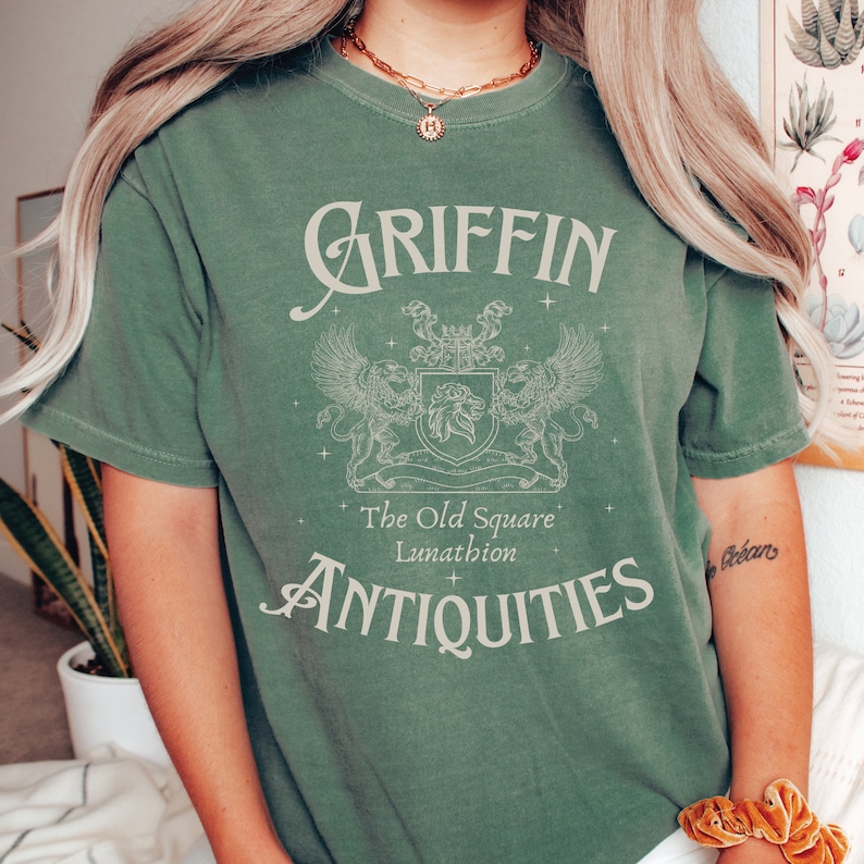 May include: A green t-shirt with a vintage-style graphic of a griffin, a crest, and the text "Griffin The Old Square Lunathion Antiques".