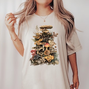 May include: A white t-shirt with a vintage illustration of a variety of mushrooms in shades of brown, red, yellow, and green.