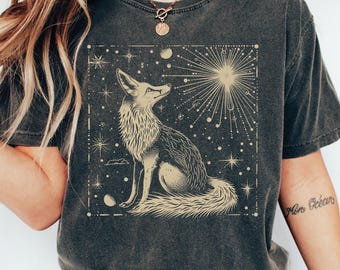 May include: A dark gray t-shirt with a graphic print of a fox looking up at a starburst. The fox is outlined in gold and the background is a dark navy blue with gold stars.