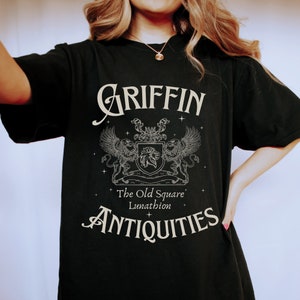 May include: Black t-shirt with a white graphic design of a griffin with the text "Griffin The Old Square Lunathion Antiques".