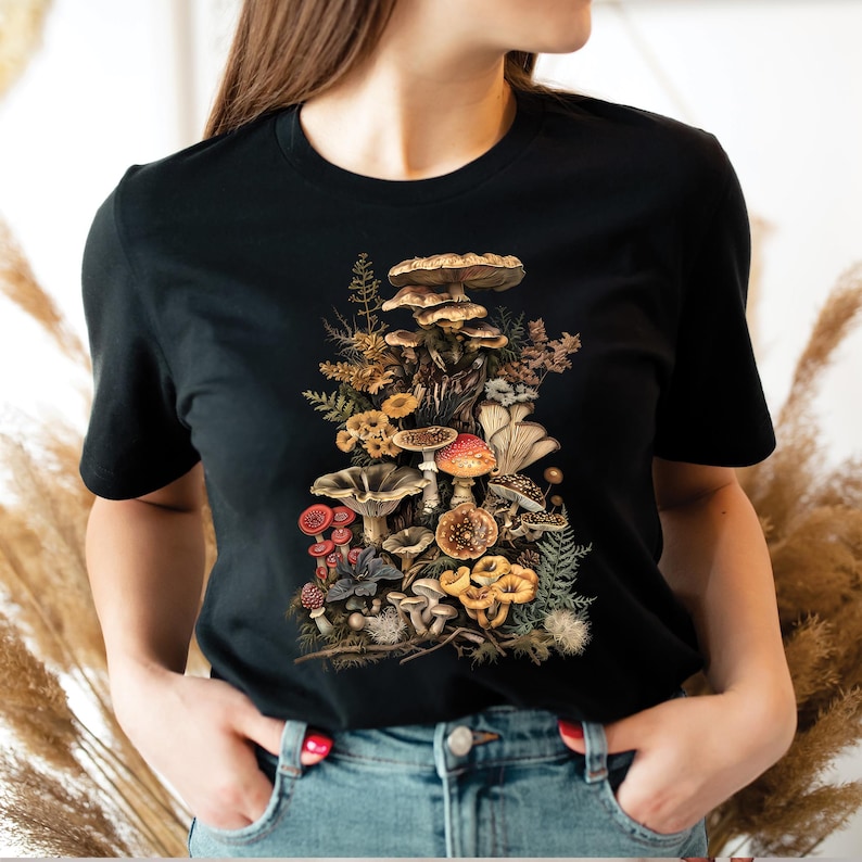 May include: Black t-shirt with a colorful illustration of a variety of mushrooms in a forest setting.