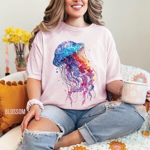 Peut inclure: Un t-shirt rose avec un motif de m&eacute;duse aquarelle color&eacute;. La m&eacute;duse est bleue, violette, rose et orange. Le t-shirt est ample et a un col rond.
