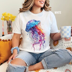 Peut inclure: Un t-shirt blanc avec un motif de m&eacute;duse aquarelle color&eacute;. La m&eacute;duse est bleue, violette, rose et orange. Le t-shirt a un col rond et des manches courtes. Le mot "WHITE" est imprim&eacute; dans le coin sup&eacute;rieur droit de l'image.