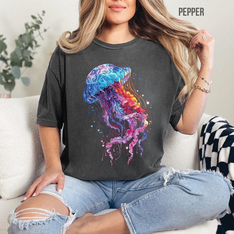 Peut inclure: Une femme portant un t-shirt gris fonc&eacute; avec un motif de m&eacute;duse color&eacute;. La m&eacute;duse est bleue, violette, rose et orange. Le t-shirt est ample et a un aspect vintage.