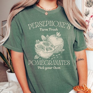May include: A green t-shirt with the text "Persephone's Farm Fresh Pomegranates Pick your own" and a drawing of pomegranates.