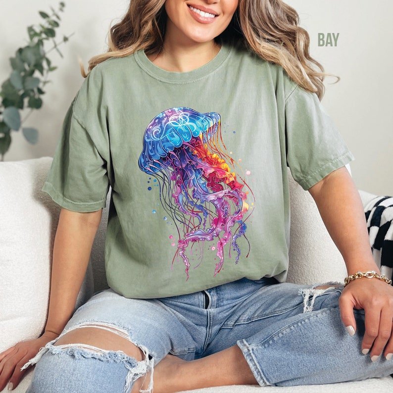 Peut inclure: Un t-shirt vert avec un motif de m&eacute;duse color&eacute;. La m&eacute;duse est bleue, violette, rose et orange. Le t-shirt a une coupe d&eacute;contract&eacute;e et des manches courtes.