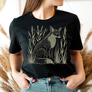 K&ouml;nnte beinhalten: Ein schwarzes T-Shirt mit einem grafischen Aufdruck eines Fuchses, der in hohem Gras sitzt. Der Fuchs ist in hellgr&uuml;n umrandet.