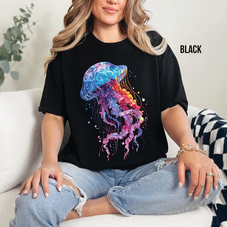 Peut inclure: Un t-shirt noir avec un motif de m&eacute;duse color&eacute;. La m&eacute;duse est d'un bleu, violet et orange vifs avec un contour blanc. L'arri&egrave;re-plan du motif est noir avec des points blancs.