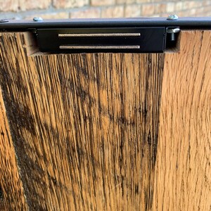 May include: Close-up of a wooden surface with a black metal frame and two silver metal strips. The wood has a dark brown stain and a natural wood grain.