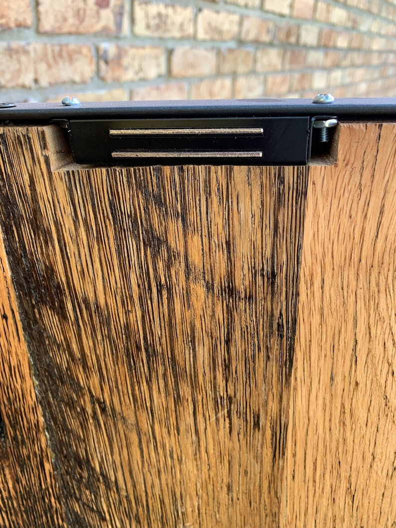 May include: Close-up of a wooden surface with a black metal frame and two silver metal strips. The wood has a dark brown stain and a natural wood grain.
