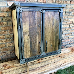 May include: A rustic wooden cabinet with two doors, featuring a black metal frame and hardware. The cabinet has a distressed wood finish and is accented with metal rivets.
