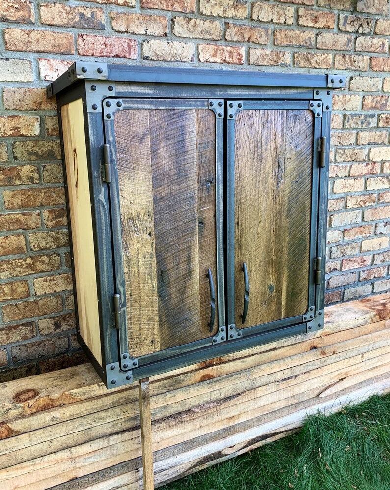 May include: A rustic wooden cabinet with two doors, featuring a black metal frame and hardware. The cabinet has a distressed wood finish and is accented with metal rivets.