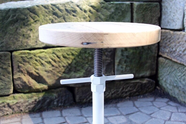 May include: White adjustable stool with a round wooden seat and a metal base. The base has a white finish and a screw mechanism for adjusting the height.