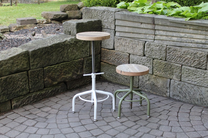 K&ouml;nnte beinhalten: Zwei h&ouml;henverstellbare Hocker mit Holzsitzen. Der Hocker links ist wei&szlig; und der Hocker rechts ist gr&uuml;n.