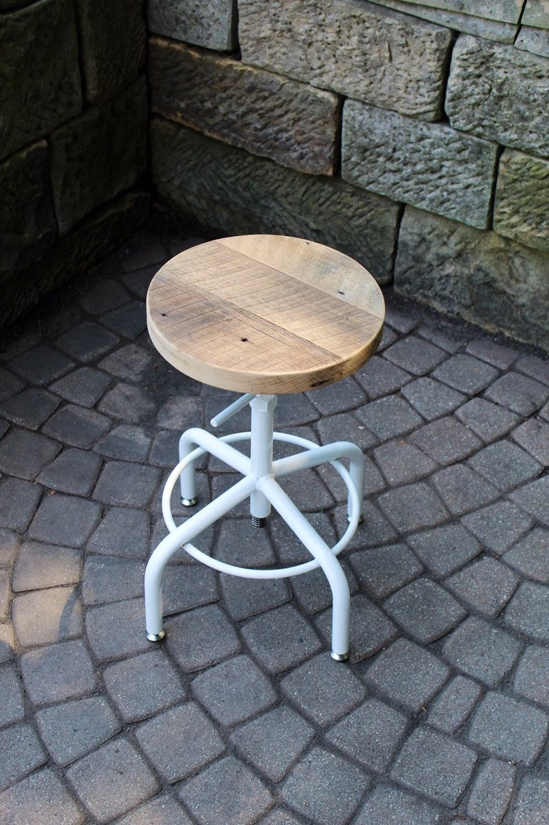 May include: A white metal swivel stool with a wooden seat. The seat is made of reclaimed wood and has a natural finish. The stool is sitting on a grey brick patio.