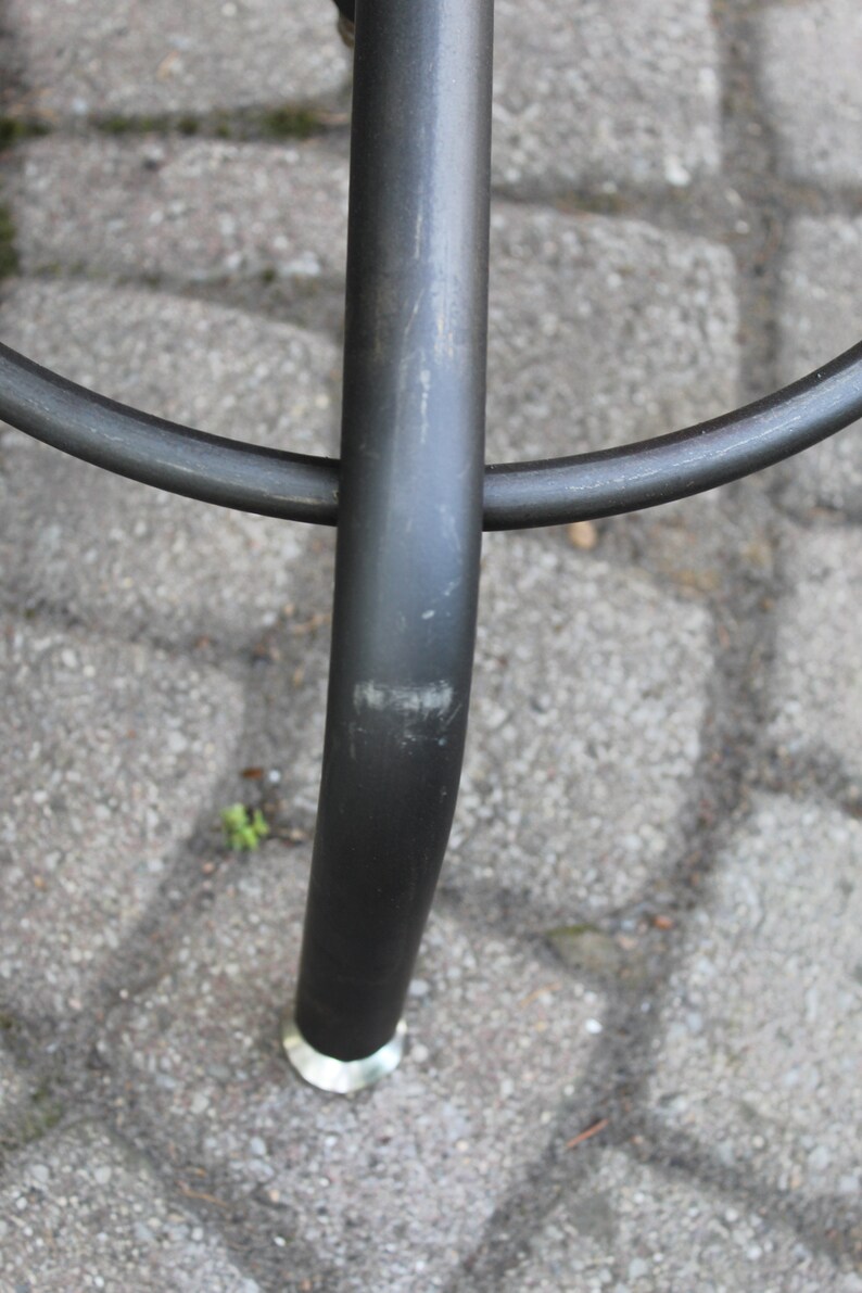 K&ouml;nnte beinhalten: Nahaufnahme eines schwarzen Metall-Barhockerbeins mit einer silbernen Fu&szlig;kappe. Das Hockerbein ist zerkratzt und weist Gebrauchsspuren auf.