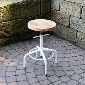 May include: White metal adjustable stool with a wooden top. The stool is sitting on a grey brick patio.