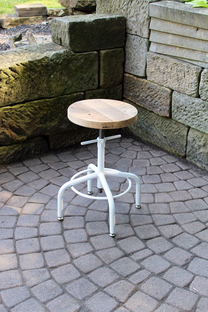 May include: White metal adjustable stool with a wooden top. The stool is sitting on a grey brick patio.