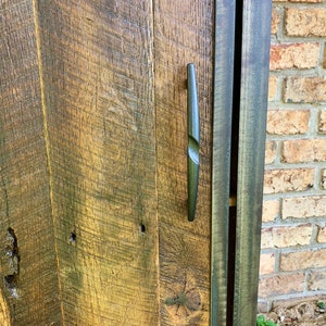 May include: A rustic wooden cabinet door with a dark brown finish. The door features a metal handle with a unique design. The cabinet is made from reclaimed wood and has a distressed look.
