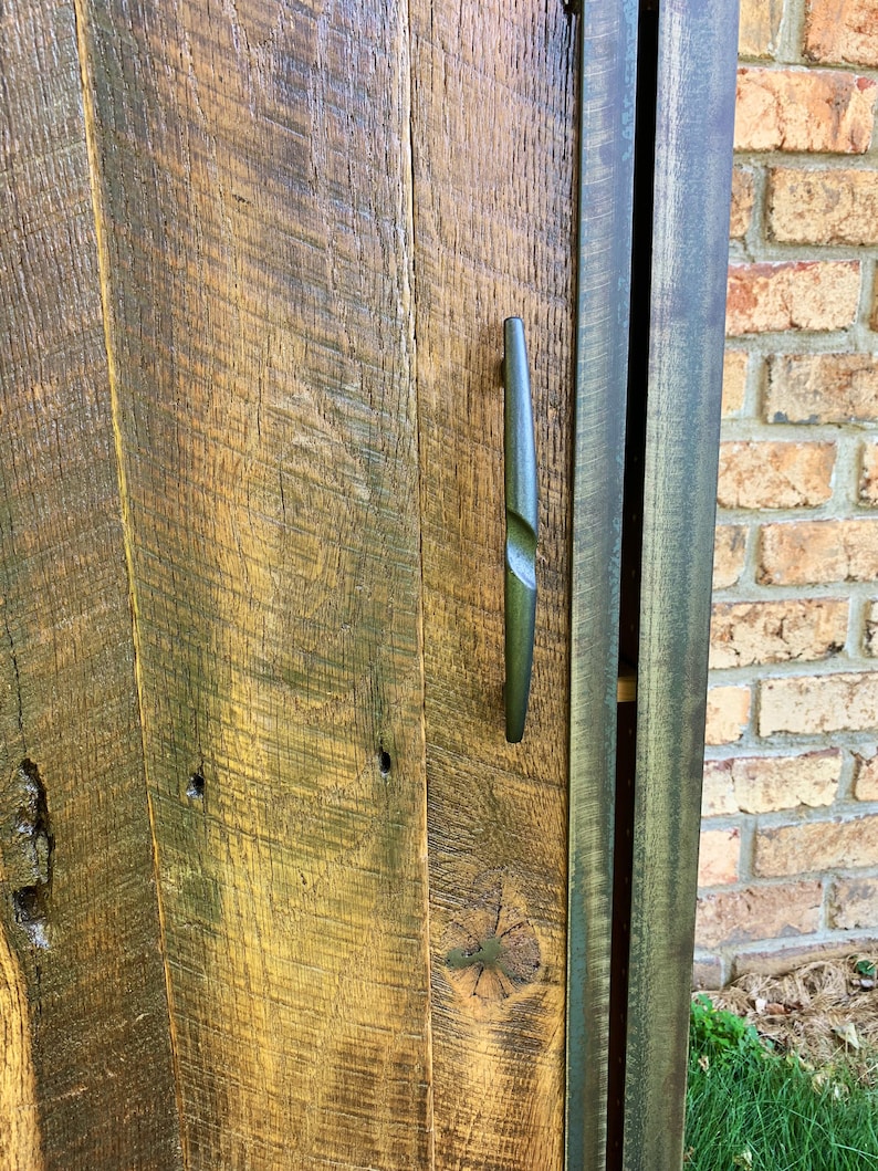 May include: A rustic wooden cabinet door with a dark brown finish. The door features a metal handle with a unique design. The cabinet is made from reclaimed wood and has a distressed look.