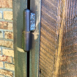 May include: Close-up of a black metal hinge attached to a wooden door. The hinge is partially open, revealing the metal pin and the wood grain of the door.