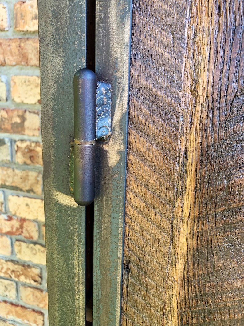 May include: Close-up of a black metal hinge attached to a wooden door. The hinge is partially open, revealing the metal pin and the wood grain of the door.