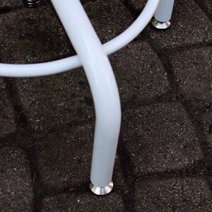 May include: White metal stool with a round seat and three legs. The legs have a white powder coat finish and silver metal feet.