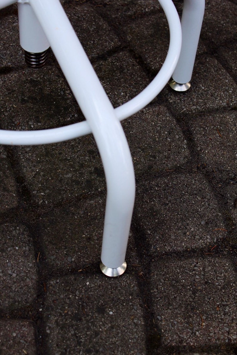 May include: White metal stool with a round seat and three legs. The legs have a white powder coat finish and silver metal feet.