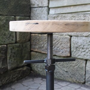 K&ouml;nnte beinhalten: Ein verstellbarer Hocker aus schwarzem Metall mit einer runden Holzfl&auml;che. Der Hocker verf&uuml;gt &uuml;ber einen Schraubmechanismus aus Metall zur H&ouml;henverstellung.