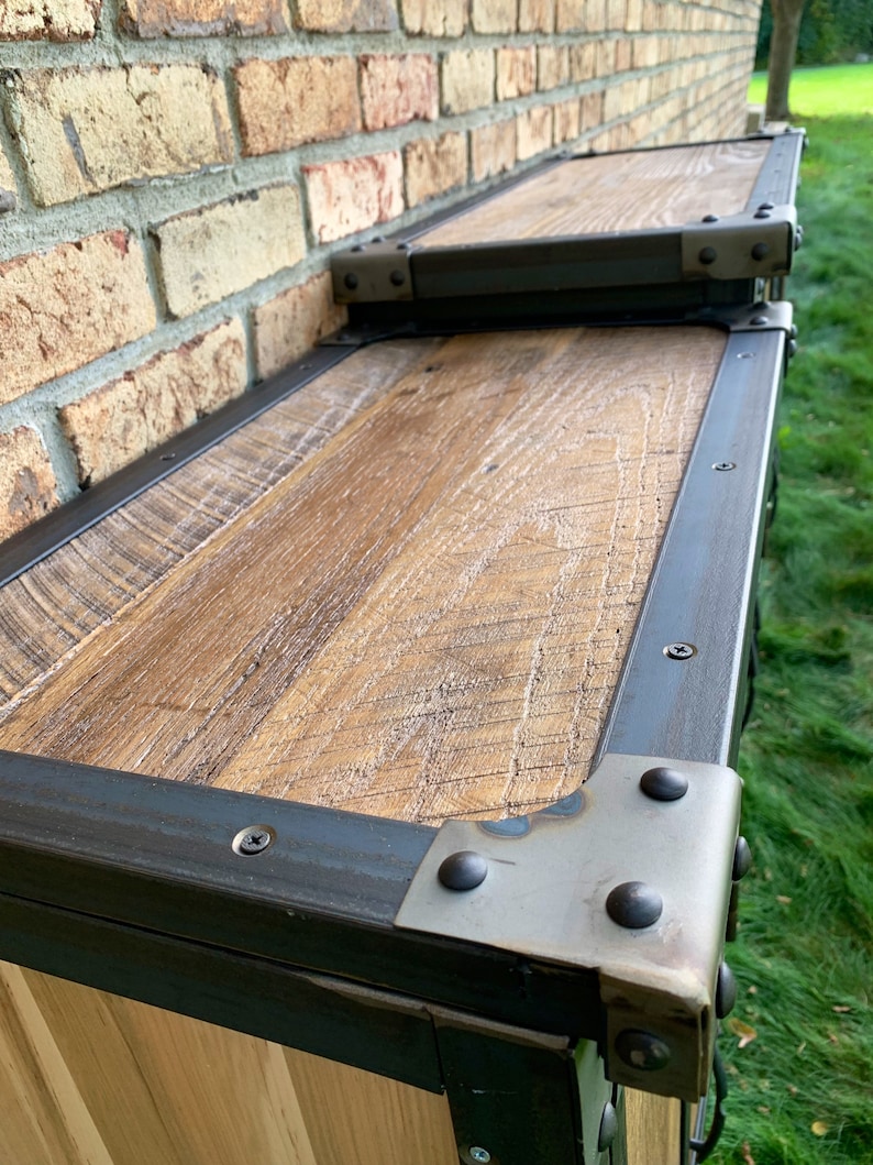May include: A wooden cabinet with a black metal frame and metal corner brackets. The cabinet has a rustic wood finish and is made of reclaimed wood.