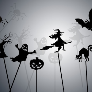 Puede incluir: Un conjunto de títeres de sombras de Halloween, que incluye una bruja en una escoba, un fantasma, una calabaza, un murciélago, una araña, un árbol y un gato negro. Los títeres son siluetas negras sobre un fondo gris claro.