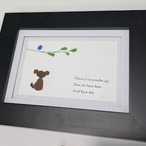 May include: A framed art print featuring a brown dog illustration with a blue bird and green leaves. The print includes the text "There is no greater joy than to have been loved by a dog." The frame is black.