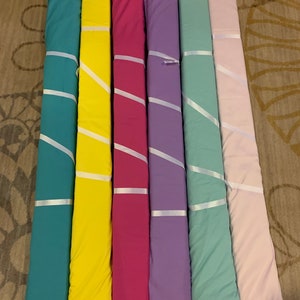 May include: Seven rolls of fabric in various colors, including teal, yellow, pink, purple, light green, and light pink. The fabric is rolled up and tied with white ribbon. The fabric is displayed on a wooden surface.
